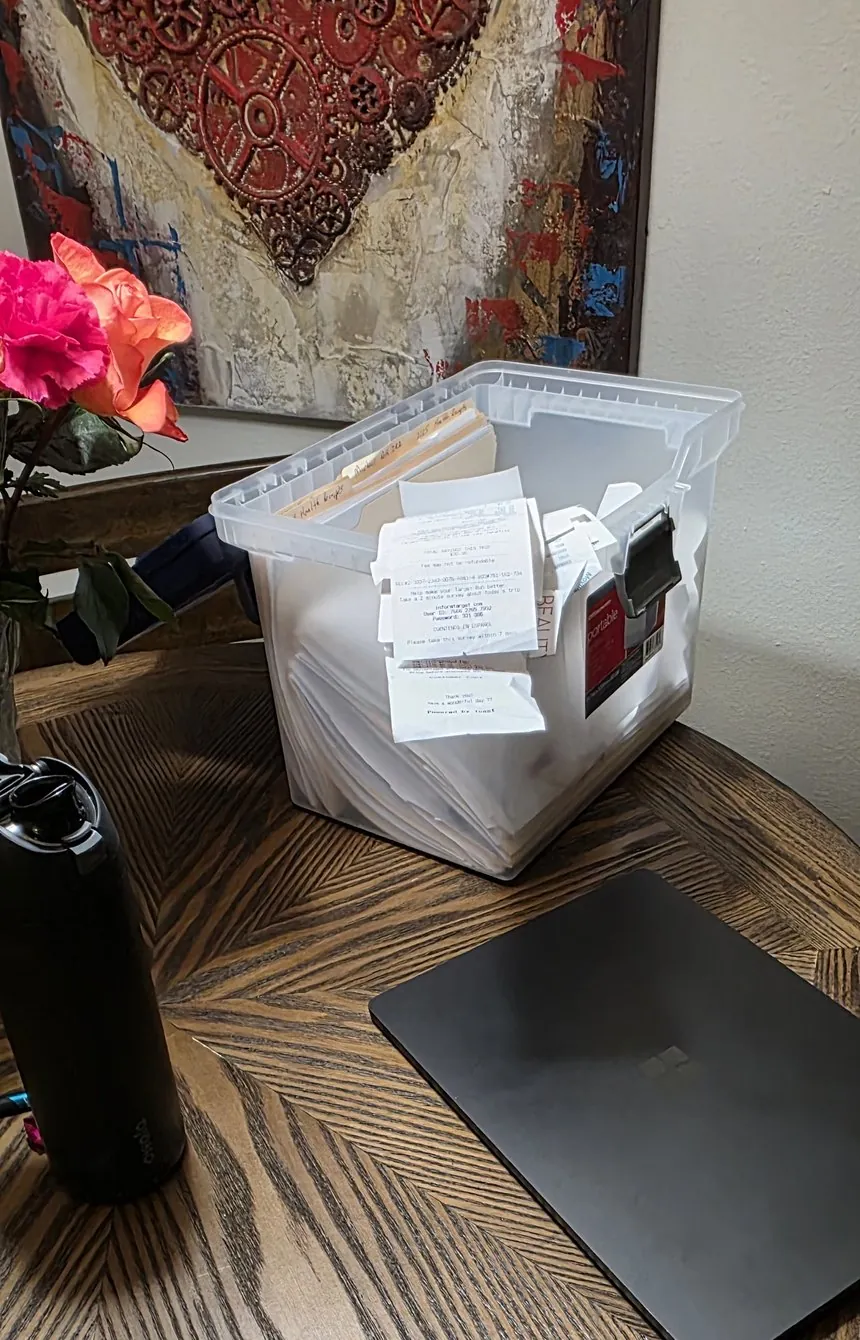 A bin overflowing with receipts and paperwork next to a closed laptop.